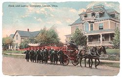 Postcard depicting fire fighters walking along a horse drawn fire wagon